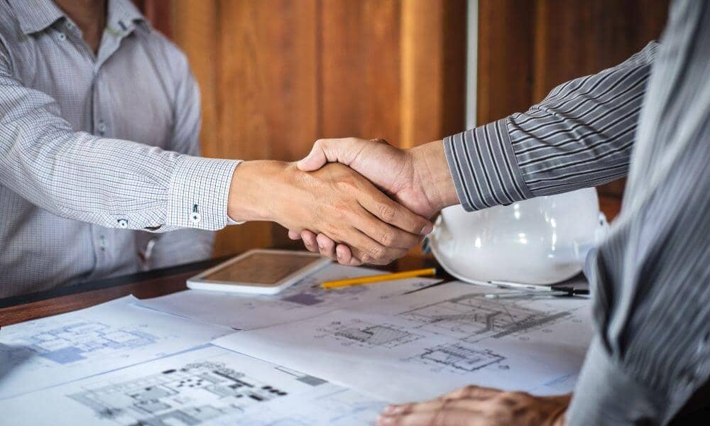 flood elevation certificate surveyor collaboration - ALTA Survey Alabama Two professionals shaking hands over construction plans, symbolizing collaboration on a certified Flood Elevation Certificate before building in Troy AL.