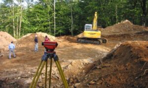 Surveyor using a total station on uneven terrain to collect elevation data for topographic surveys before site development