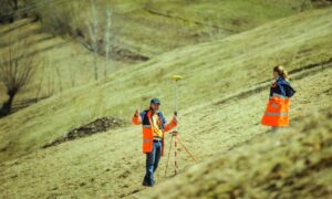 Surveyors conducting a topographic survey on sloped terrain to assess elevation and land features before development.