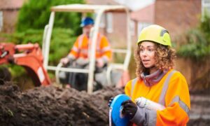 Female civil engineering professional in safety gear assessing a construction site with excavation equipment in the background