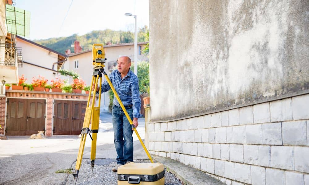 Land surveyor using a total station to perform a boundary survey after heavy rains near a residential property