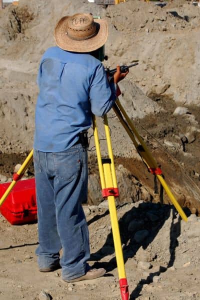 Licensed land surveyor using total station to measure property elevations in a flood-prone area
