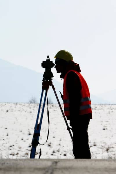 Licensed land surveyor using equipment during a closing survey to check property boundaries

