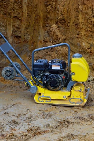 Worker using soil compaction equipment to prepare stable ground as part of grading plans for site development