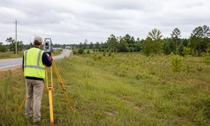 Land surveyor using a total station on vacant commercial land in Birmingham, AL for an ALTA survey